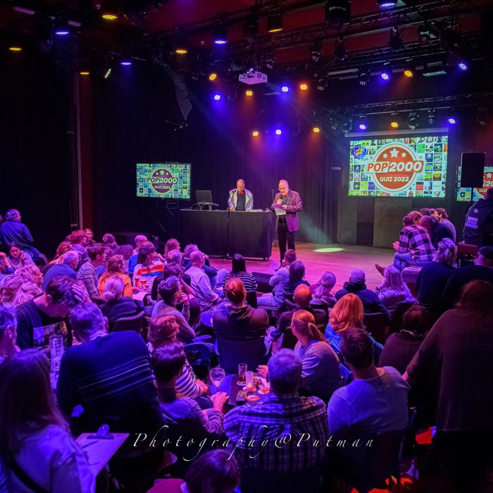 Afbeelding van publiek en presentator in actie tijdens de Top 2000 Quiz.