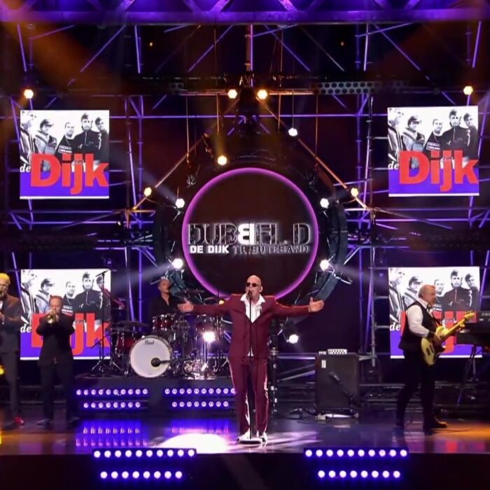 De Dijk tribute act performt op het podium bij tv-paogramma Battle of the bands, zanger draagt bordeau-rood pak.