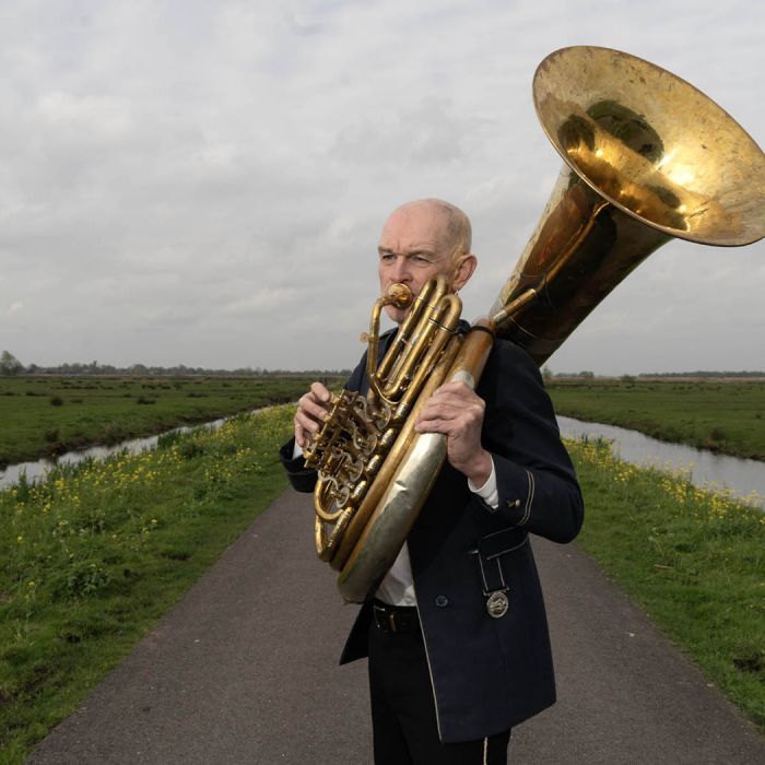 Bandlid De Kift met groot blaasinstrument op straat