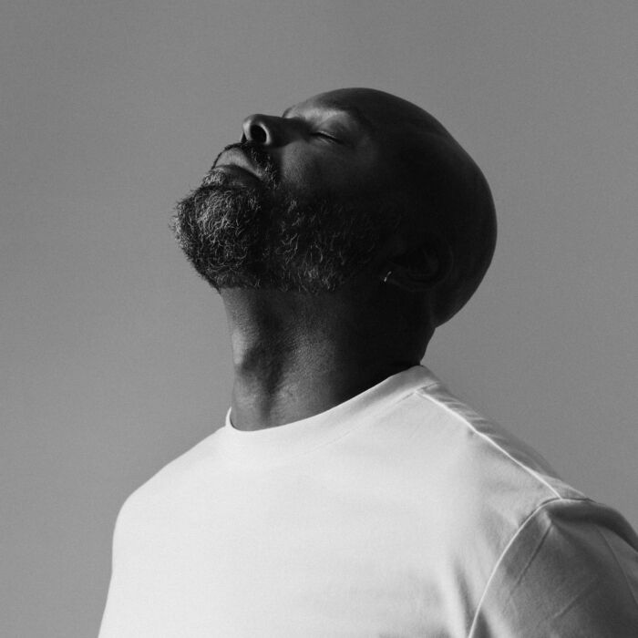 Artiest Myles Sanko poseert met ogen dicht voor een grijze achtergrond