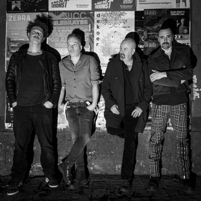 Bandleden Radio Clash Belgium hangen stoer tegen een muur en kijken in de camera.