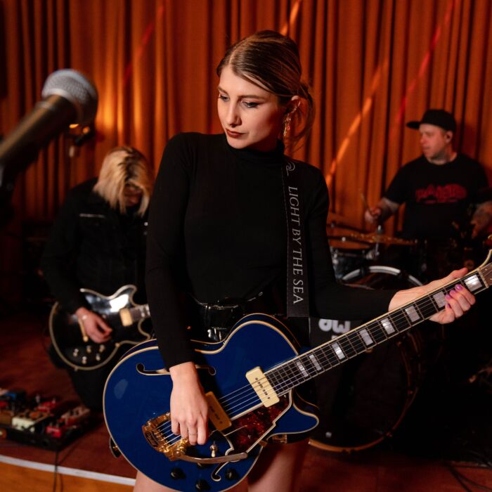 Frontvrouw van Lights By The Sea poseert in zwarte outfit en met elektrische gitaar in de hand.