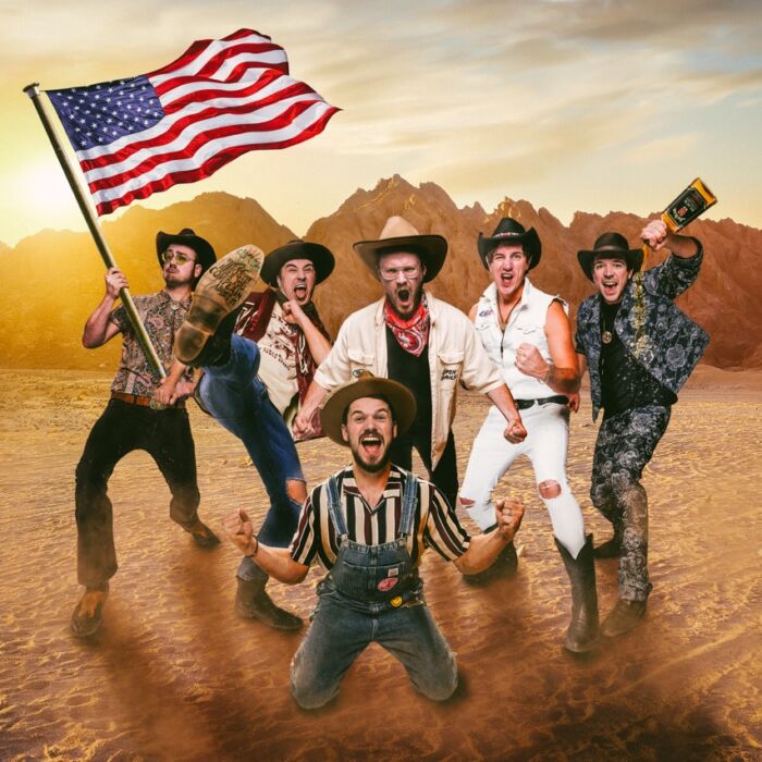 Bandleden van The Hillbilly Moonshiners poseren schreeuwend in een woestijn met Amerikaanse vlag in de hand.