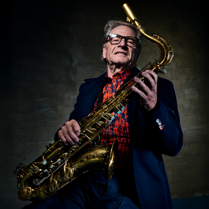 Saxofonist Hans Dulfer poseert zittend met saxofoon in de hand en kijkt in de camera