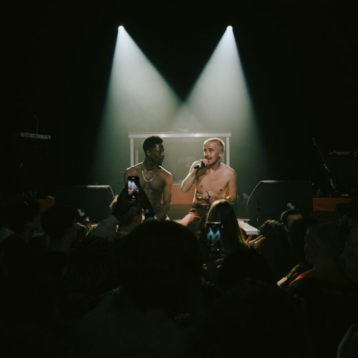 Rappers Rens & Jaïr performen met ontbloot bovenlijf voor een volle zaal, er staat een lichtspot op ze gericht.