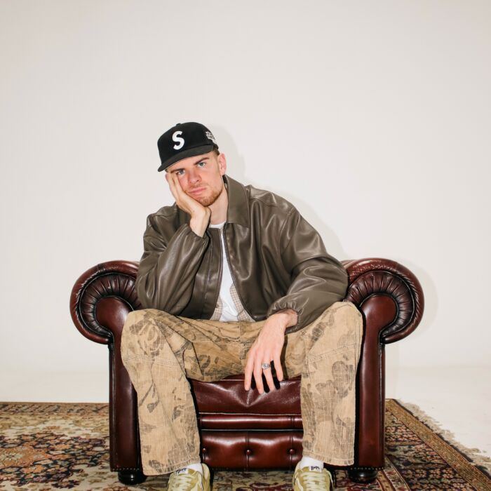 Rapper Lau leunt op zijn hand en zit op een leren stoel.