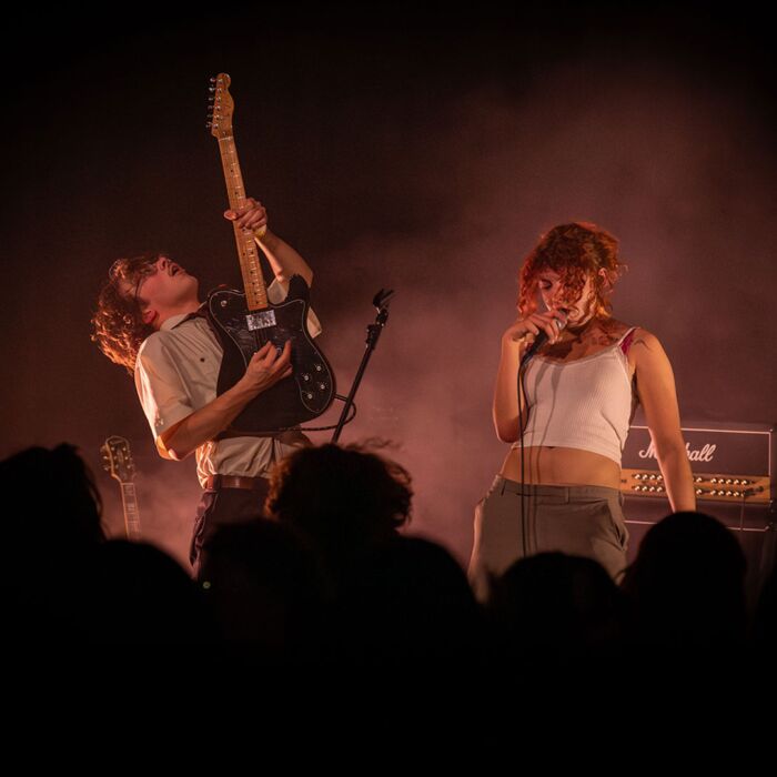 Clitteband frontvrouw en gitarist geven energieke performance op het podium terwijl een grote groep mensen toekijkt.