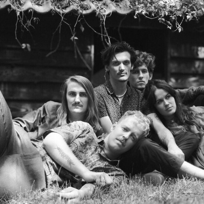 Zwartwit-foto van bandleden van De Mis, ze liggen dicht tegen elkaar op het gras en staren in de camera.