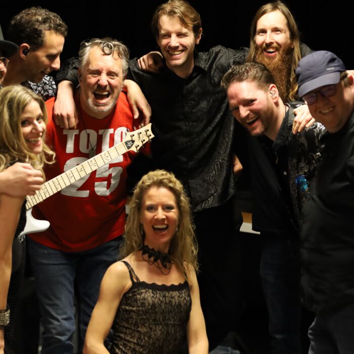 Bandleden van Kingdom of Toto houden elkaar vast en kijken lachend in de camera