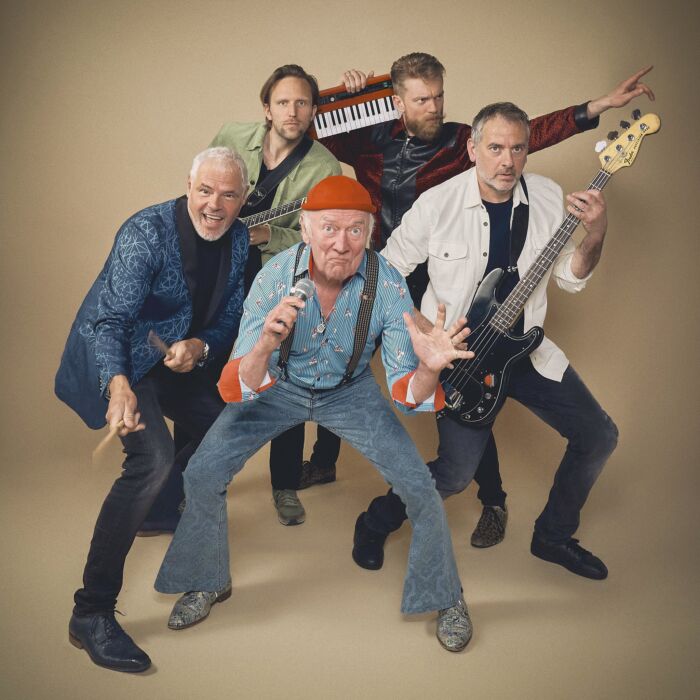 Bandleden van Drukwerk poseren vrolijk en energiek voor een beige achtergrond.