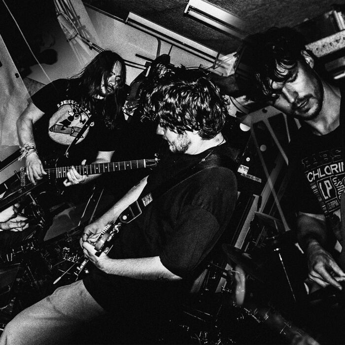 Chaotische Zwart-witfoto van rockband SERVALS, die met gitaren in hun hand staan te performen.