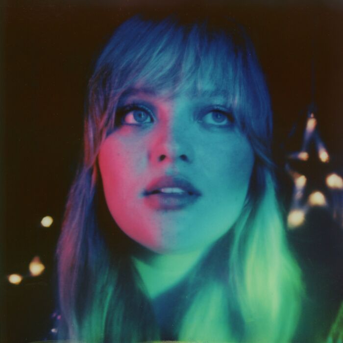 Persfoto van het hoofd van artiest Sophia, ze staart dromerig in de verte met donkere achtergrond met enkele lichtpunten.