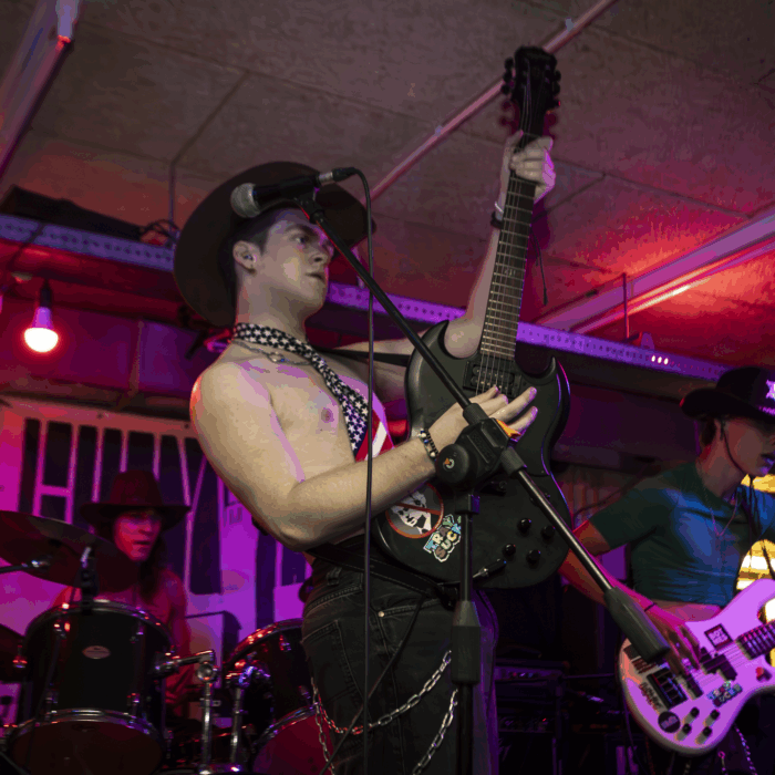 Bandlid van Tray is te zien met electrische gitaar in hand en hoed op en ontbloot bovenlijf, op de achtergrond zie je drummer en bassist hun instrument bespelen.