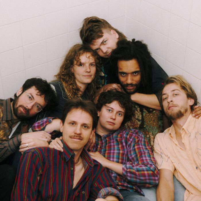 Bandleden van de Zweefclub liggen dicht tegen elkaar aan op de grond en kijken in de camera