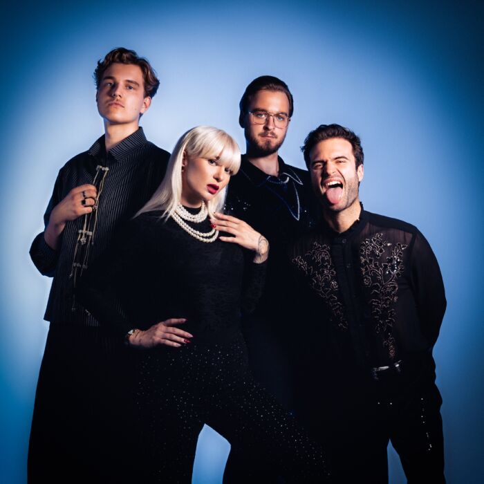 Vier bandleden van Case Candy poseren in zwarte kleding voor een blauwe achtergrond.