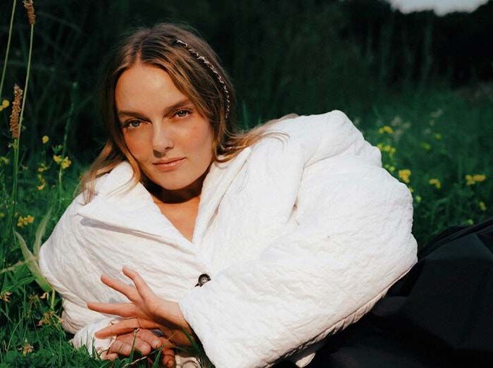 Leadzangeres van The Indien ligt in het gras, leunt op rechterzij en kijkt in de camera.