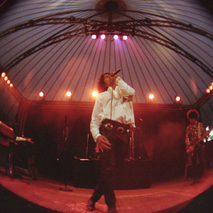 Vocalist van The Doors in Concert zingt op het podium begeleid door band in witte blouse en donkere denim broek.