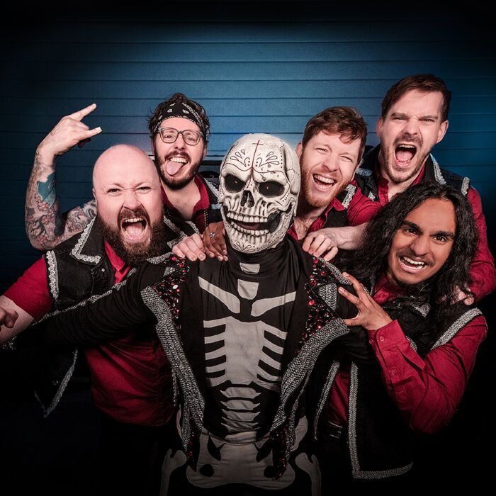 Op de foto is de band te zien met voorop iemand in een skeletten kostuum en dan de band Pene Corrida links en rechts eromheen