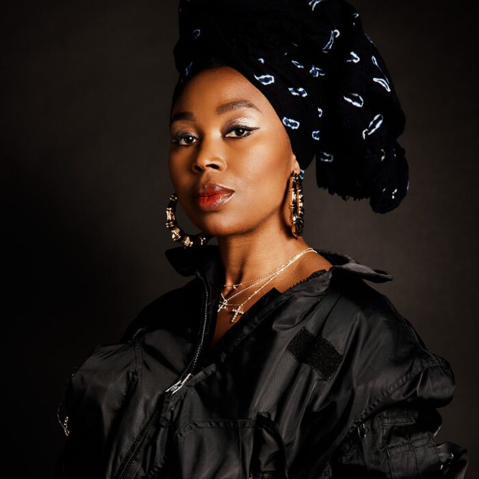 Artiest Ntjam Rosie poseeert in zwarte kleding voor de camera met handen in de zakken van haar jas.