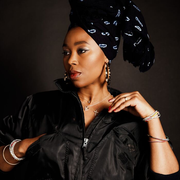 Artieste Ntjam Rosie poseert voor camera met één hand in zak van haar jack en 1 hand gebogen op schouderhoogte. Ze kijkt weg over haar rechter schouder.