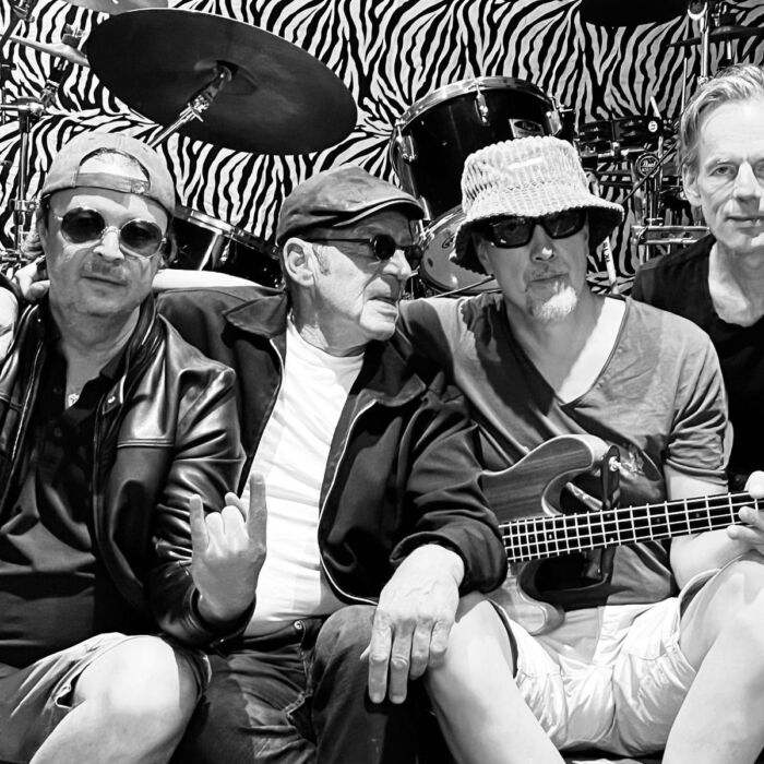 Zwart-witfoto van vier mannelijke bandleden van de band Indie Alley. Ze zitten op de grond voor een drumstel naast elkaar.