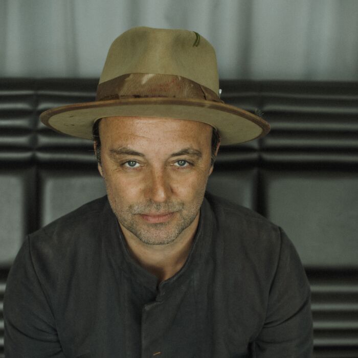 Persfoto van artiest Niels Geusebroek. Hij zit op een bankje en kijkt recht de camera in