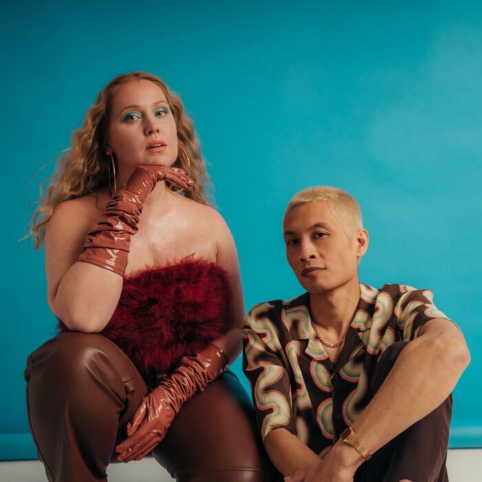 Sietske en Remi van Secret Rendezvous poseren naast elkaar voor de camera. Sietske zit op haar hurken en remi op de grond, ze kijken in de camera.