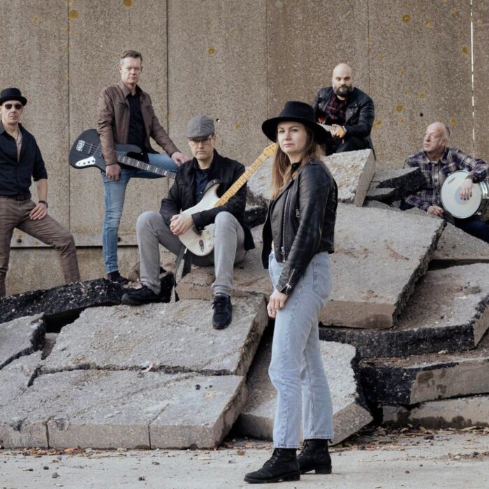 Bandleden van Next Gear poseren staand en zittend met instrumenten in de hand op een stapel grijze betonnen platte blokken.