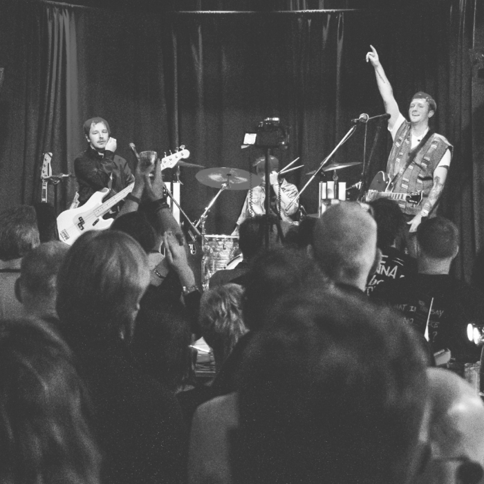 drie mannen staan op een podium en bespelen een instrument voor een vol publiek.