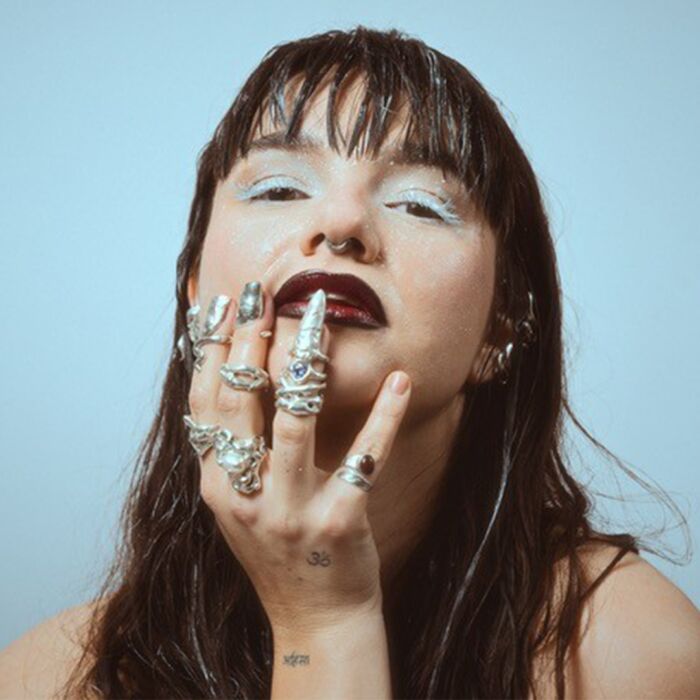 Electro-pop noir-zangeres ESSYLA poseert naakt en leunt haar kin in de palm van haar hand.