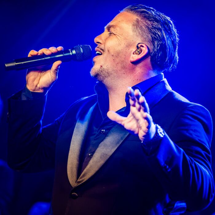 De zanger van GEWOON ANDRÉ zingt intens met zijn hand opzij uitgestrekt