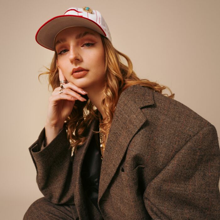 Swan kijkt in de camera met een oversized colbert aan en een baseball cap op