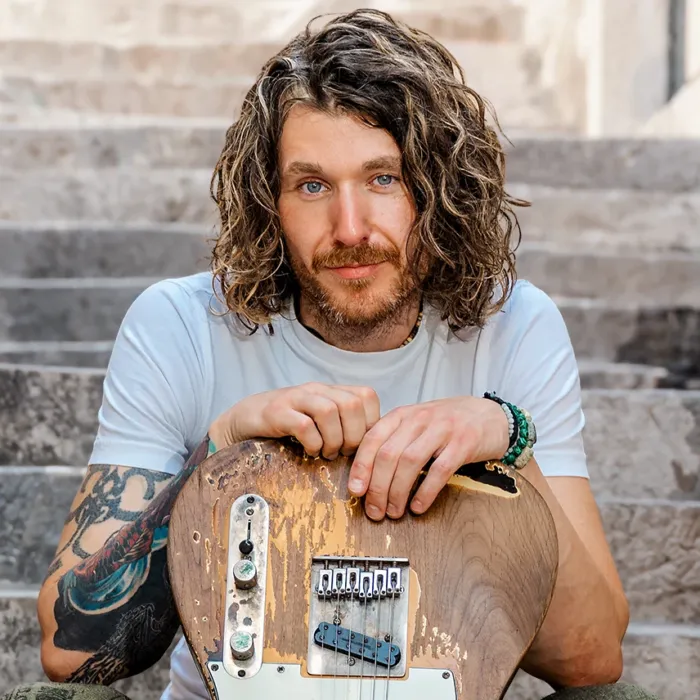 Afbeelding van Dom Martin op een trap met een gitaar vast.
